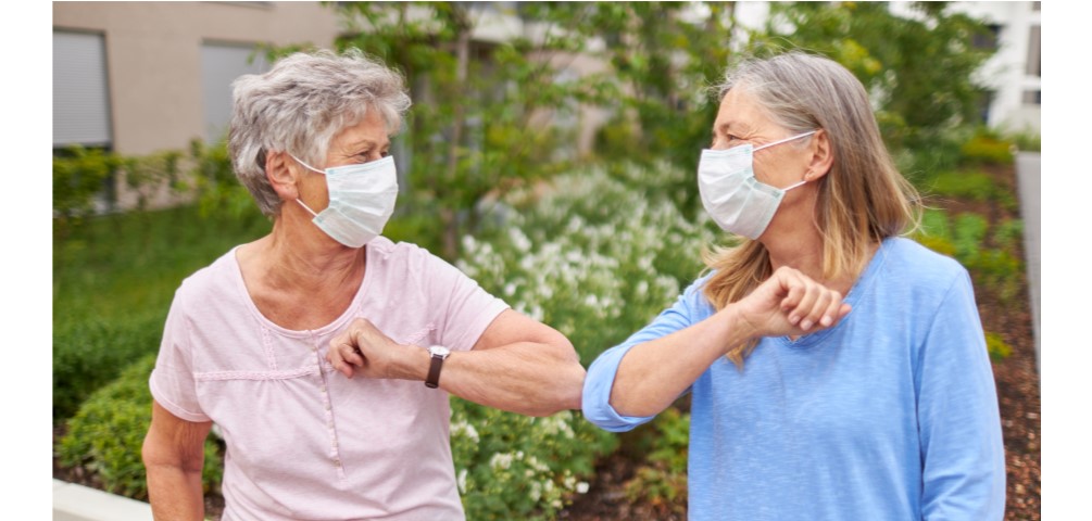 two older women wearing masks bump elbows