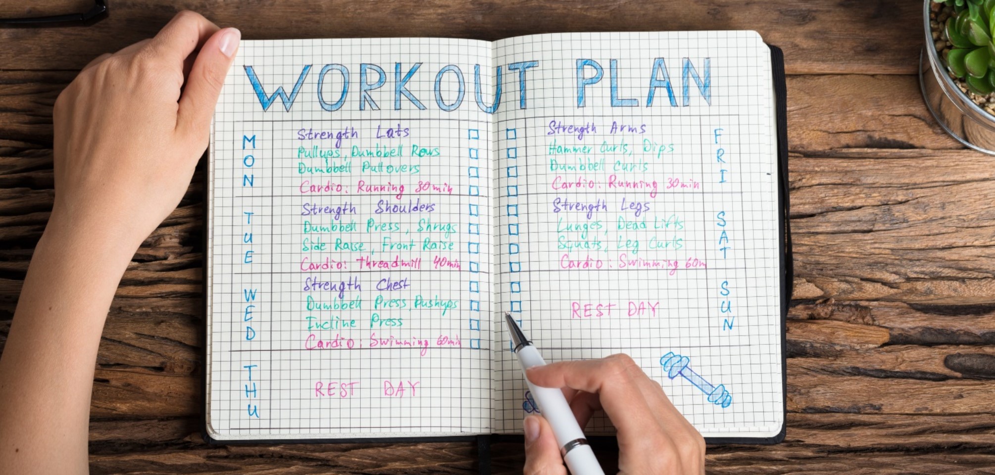 hands write into a notebook that has a workout plan outlined in it.