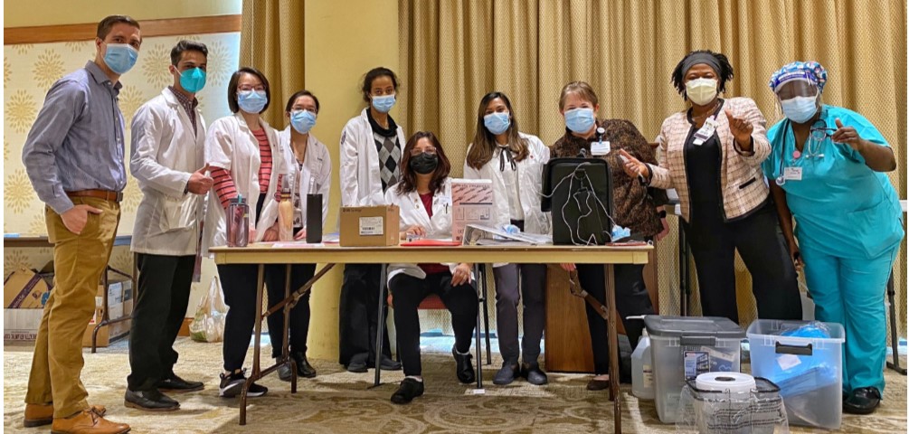 a group of health care workers in masks are around a table as they prepare to administer COVID-19 vaccines