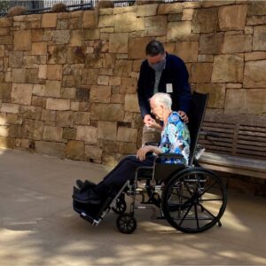 a woman in a wheel chair gets a back scratch from her son during a visit outdoors
