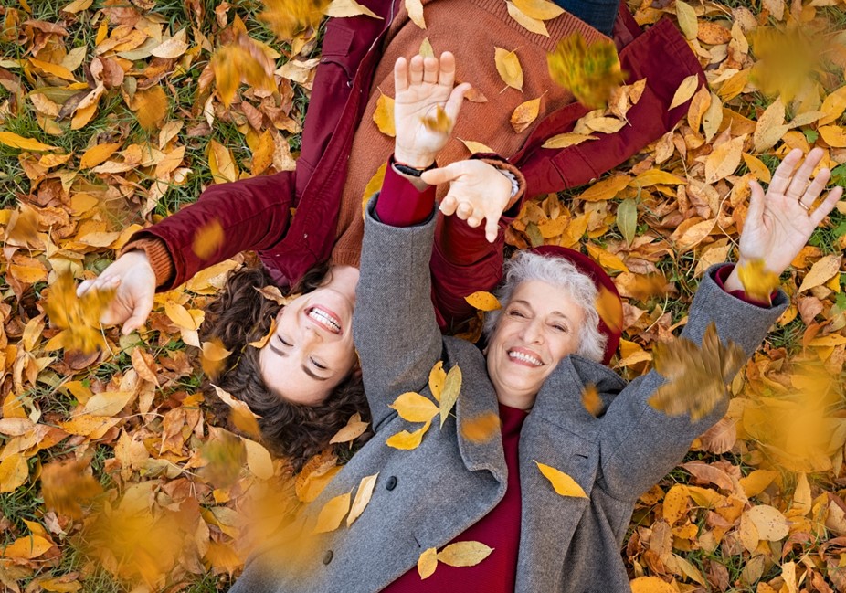 older woman and her adult daughter play in a pile of fall leaves