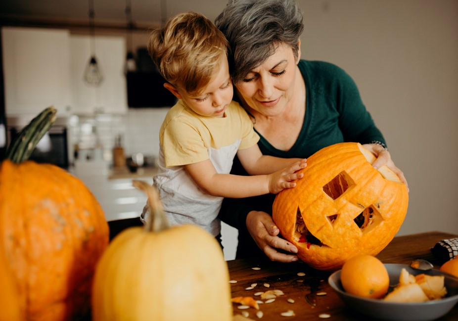 older woman carves pumpkins with young grandson