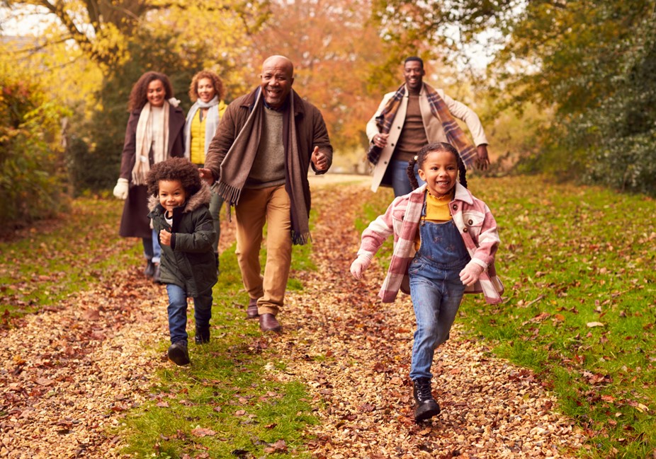 grandfather with adult children behind him runs after grandchildren outside playing in the fall.