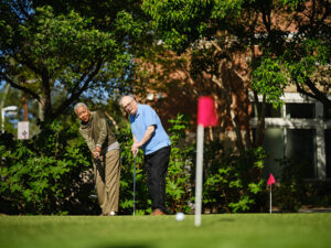 an older man and woman play putt putt outside
