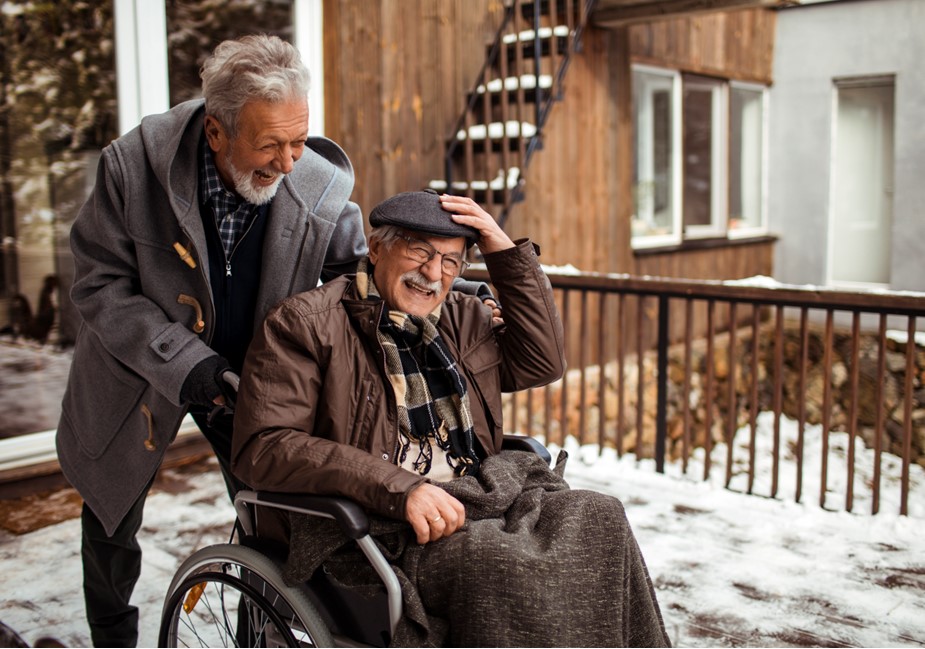 Older man pushes friend in wheelchair in Winter