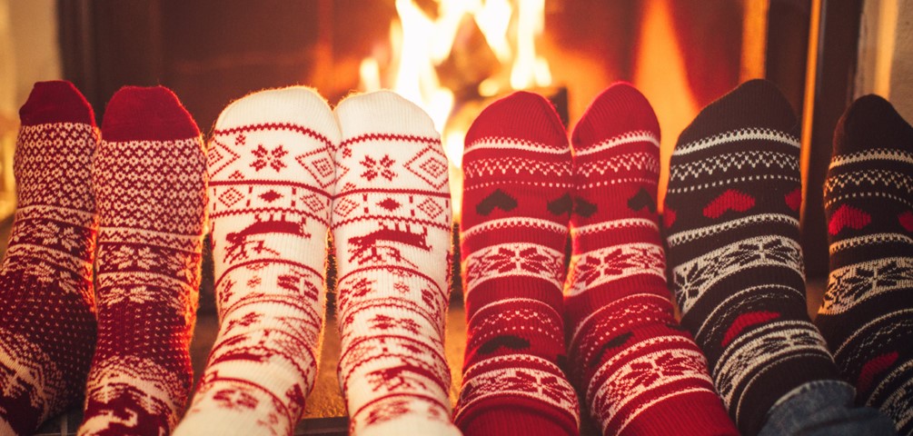four pairs of feet in cozy winter socks in front of a fireplace with a roaring fire