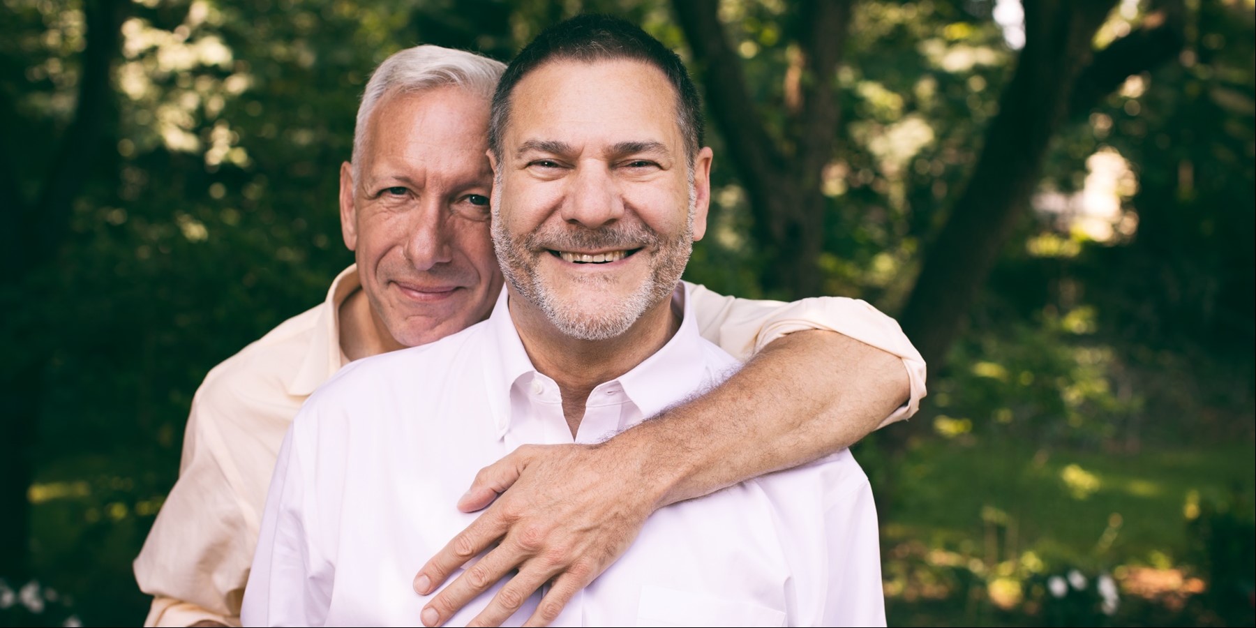 an older adult male lovingly embraces his husband as they smile