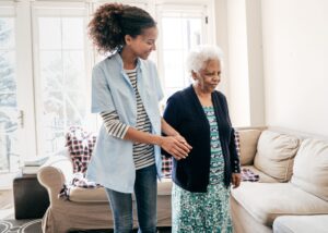 African American care partner walks with older African American woman.