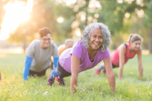 multiple older women participating in an outdoors fitness class, doing push ups