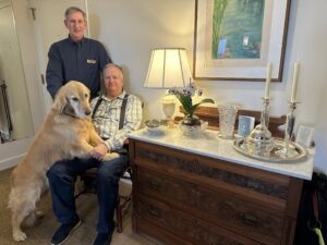Peter Ostik and Bruce Rieder pose with their golden retriever next to a sideboard in their apartment home.