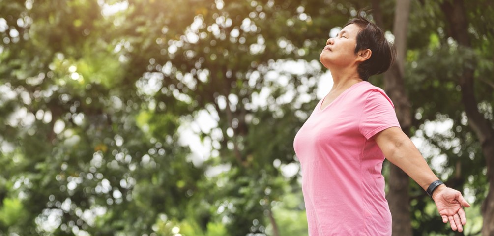 functional breath. an older woman in a pink shirt stands outside taking a deep breath