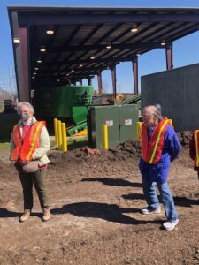 two older adults in reflective gear standing outside at a composting facility