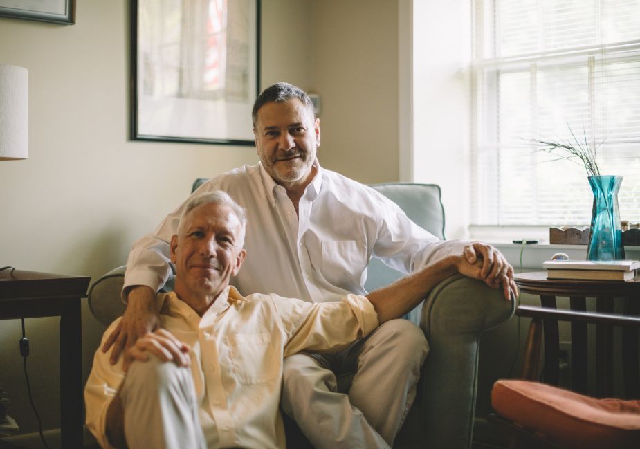 two older men sit together holding hands