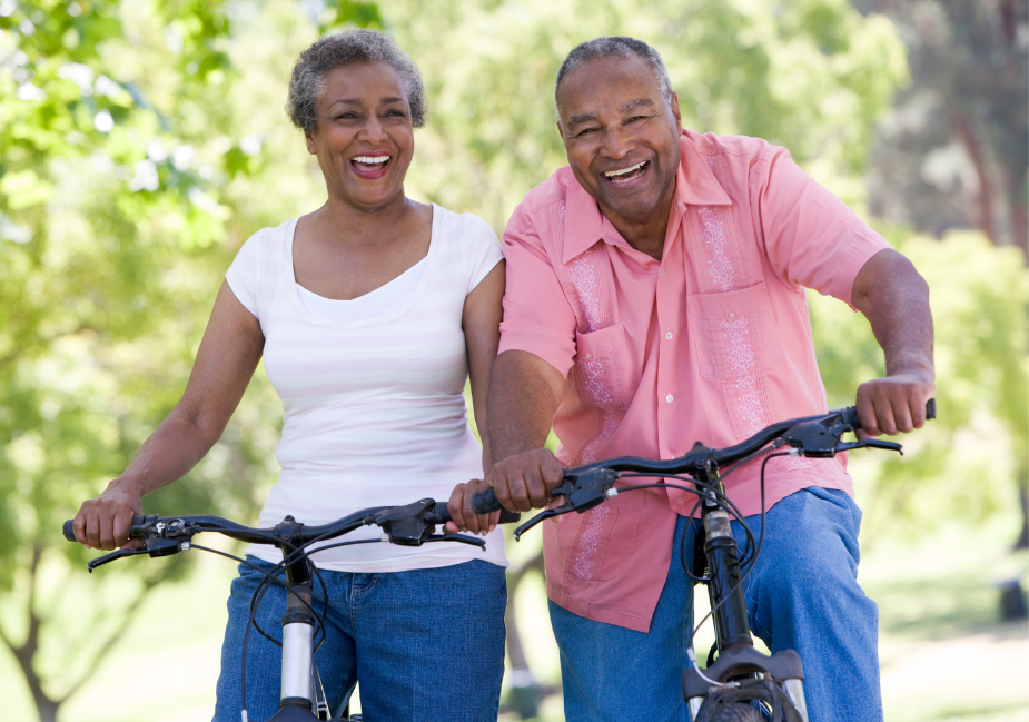 older adult woman in white shirt with older adult man in red shirt, both are biking outside