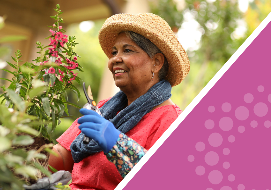 older woman wearing a hat and carrying garden shears looks at a red flower as she works in her garden
