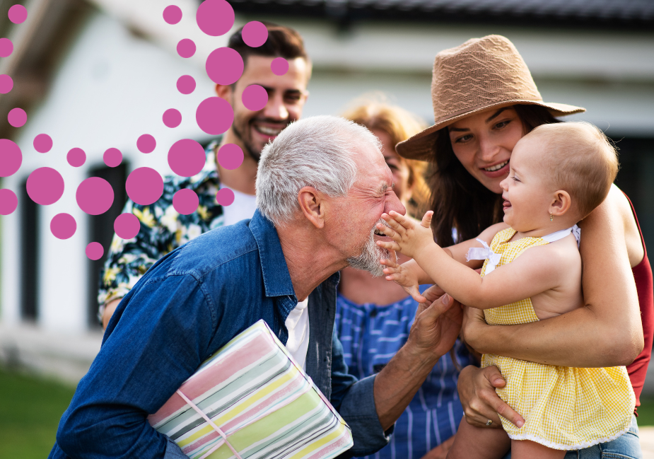 a younger woman in a yellow top and tan hat holds a baby, who is smiling at an older man and touching his face.