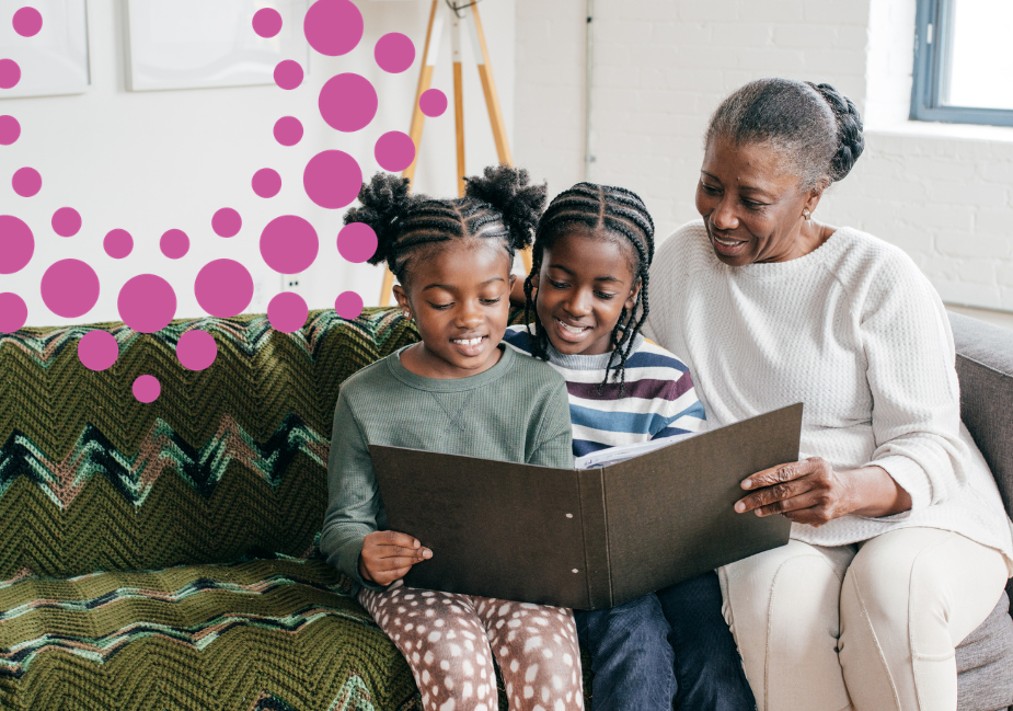 a grandmother reads a book with her two young granddaughters as they sit on a green couch together